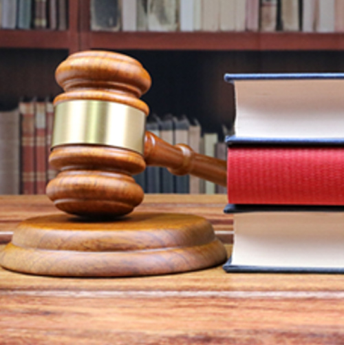 A wooden gavel resting on a wooden block with 3 books stacked next to it.