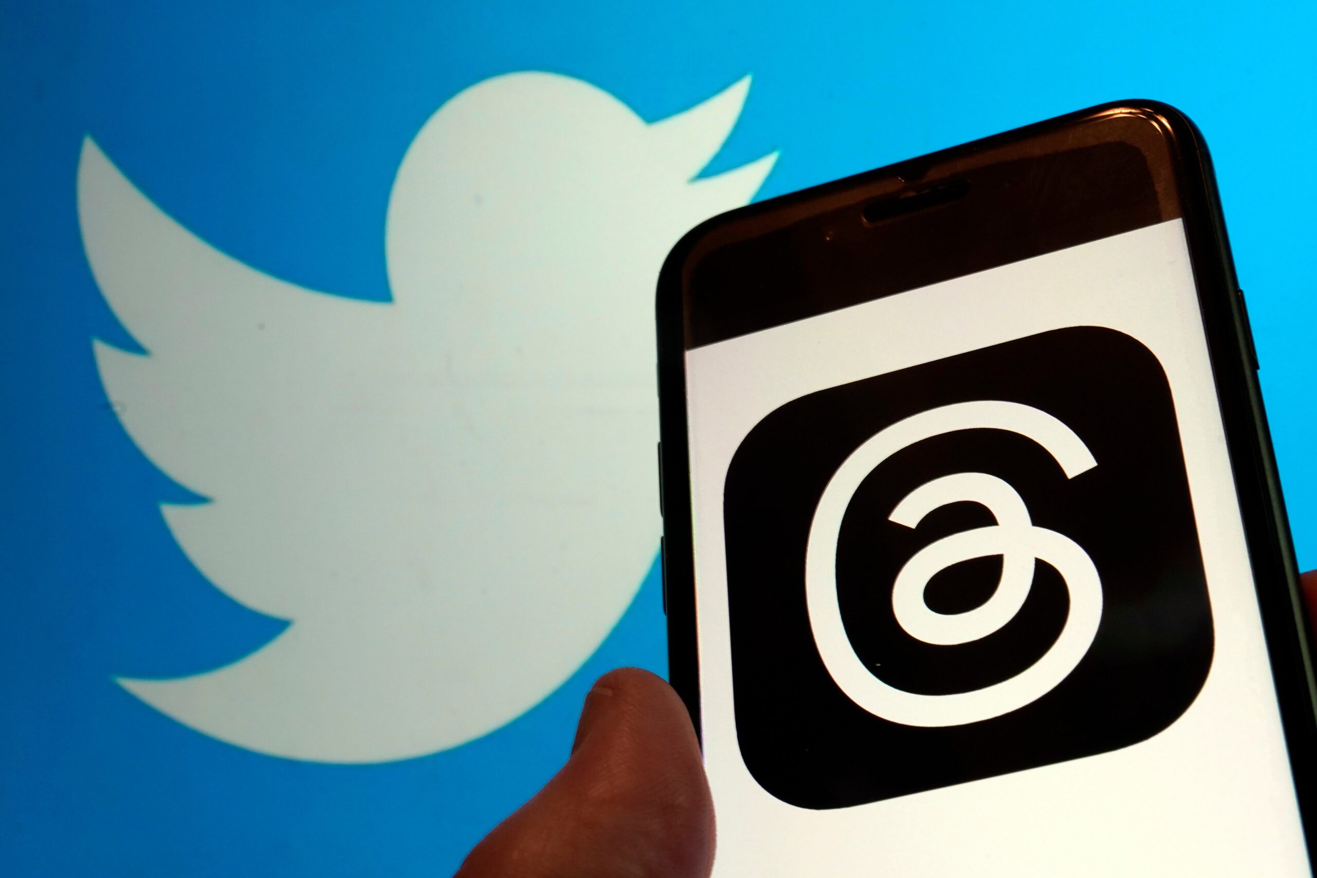 Blue Twitter bird logo next to Instagram Threads Logo on cellphone.