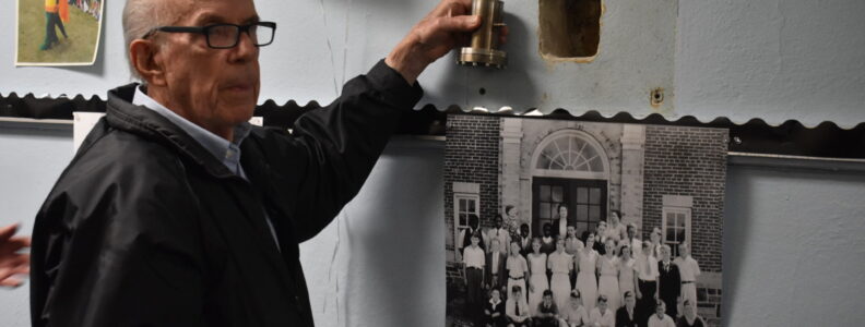 Man holding time capsule next to hole in the wall where it was stored.