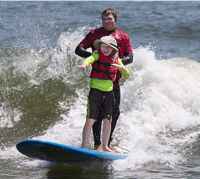 Blind youth surfer with an adult instructor gets a surfing lesson on a surf board in the ocean