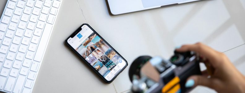 Overhead view of person using camera, cellphone open to social media, laptop and keyboard.